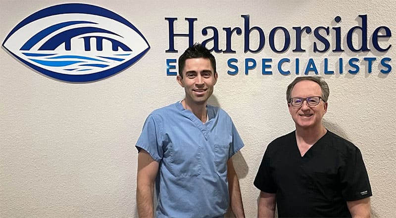 Dr. Daniel Solano and Dr. Neil Zusman in surgical scrubs in front of the Harborside Eye Specialists sign